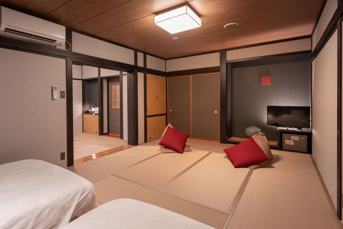 A traditional Japanese-style room with tatami flooring, two beds, a television, and a small table with a vase.