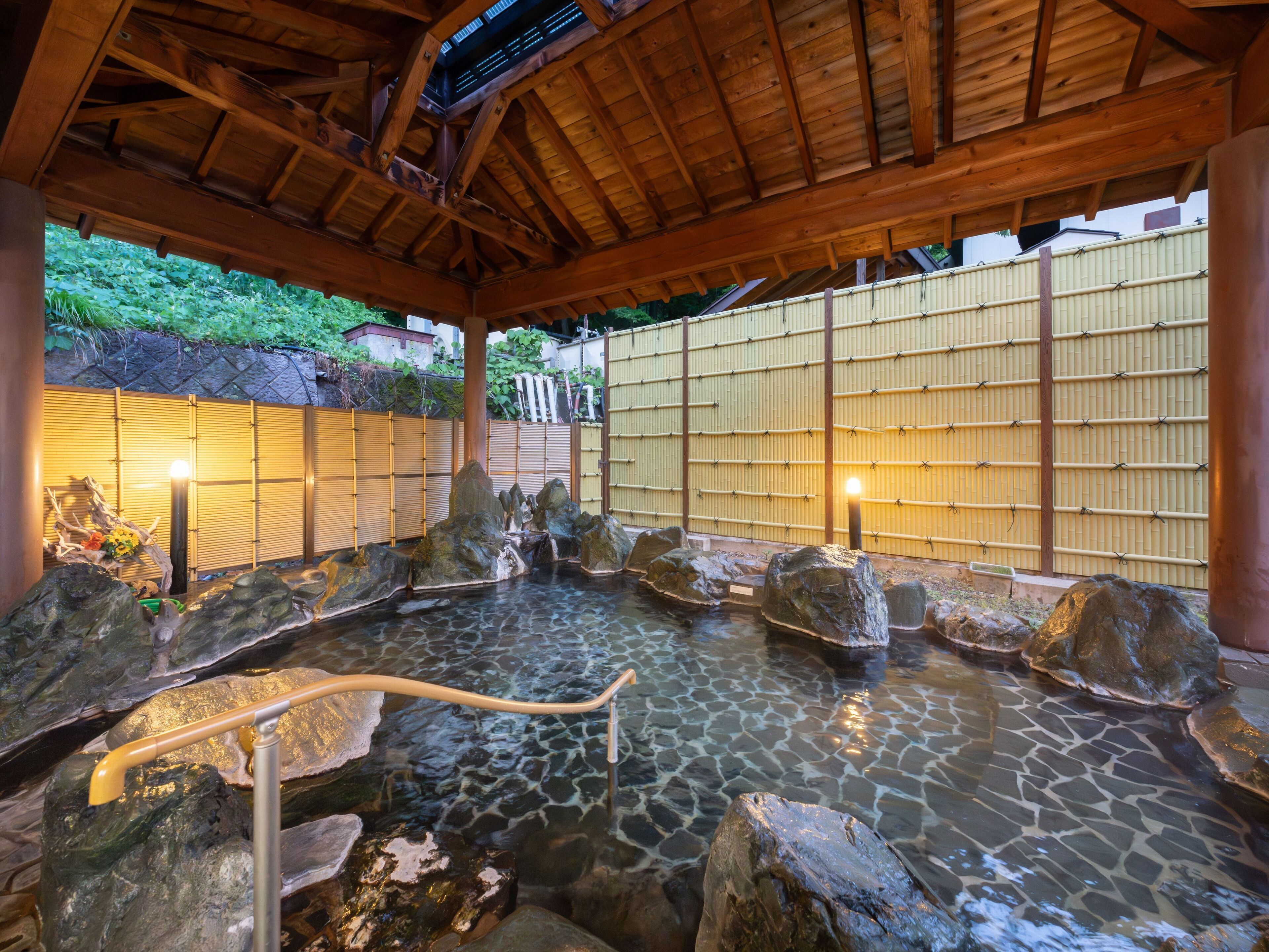 Ein traditionelles japanisches Onsen mit Steingewölbebädern, Holzbalken und Bambusverkleidungen.