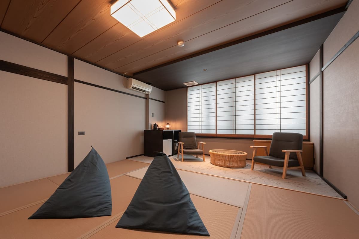 A tatami mat room with a low table, two chairs, and a large window with shoji screens.
