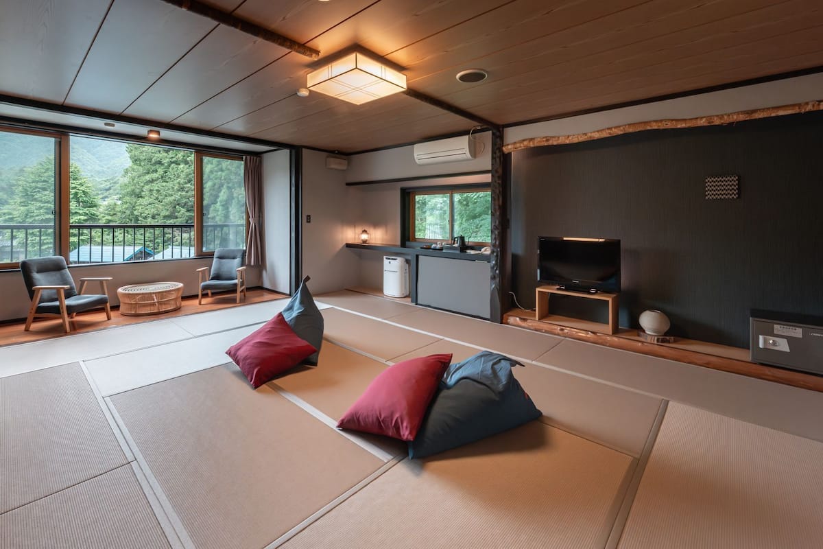 A modern room with tatami mats, a TV, a safe, and a balcony with a view of greenery.