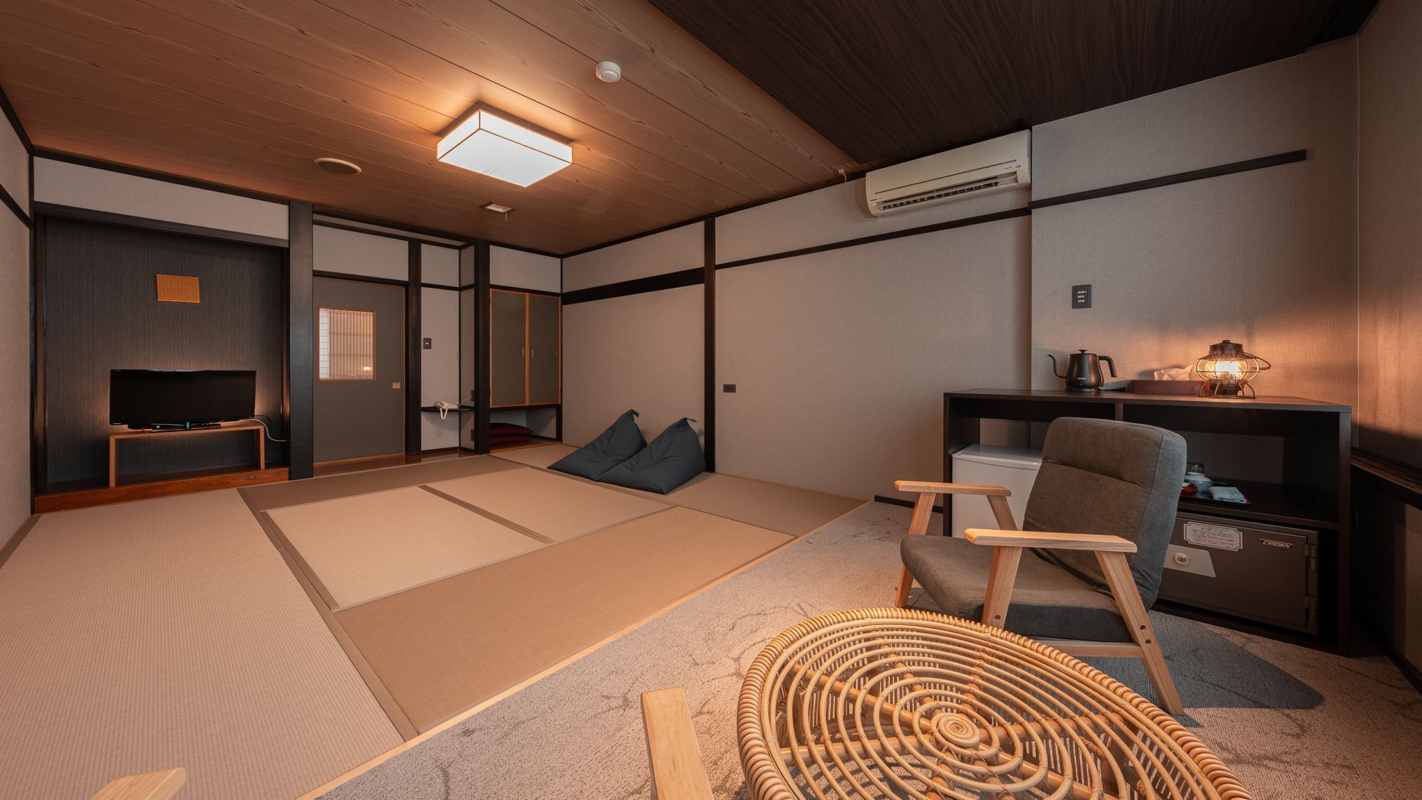 A traditional Japanese-style room with tatami flooring, a television, a sofa, a small table with a kettle, and a lamp.