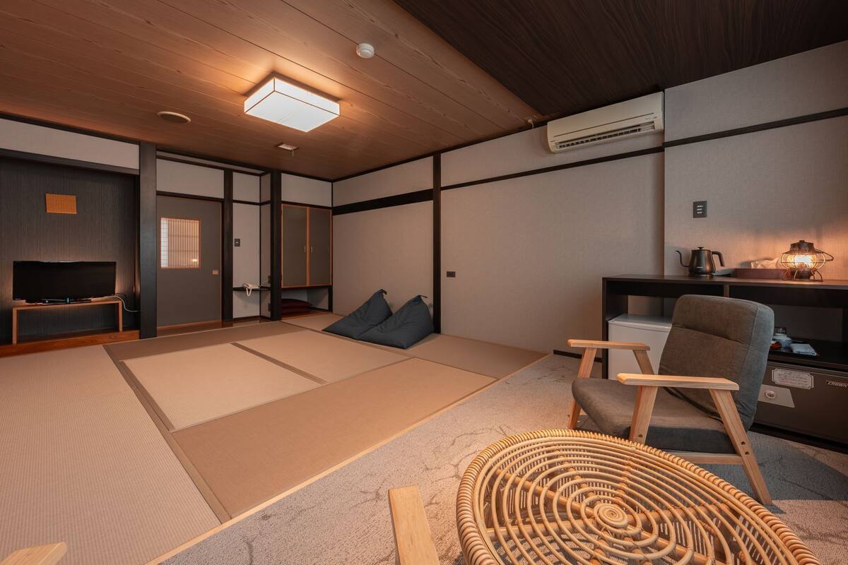 A traditional Japanese-style room with tatami flooring, a television, a sofa, a small table with a kettle, and a lamp.