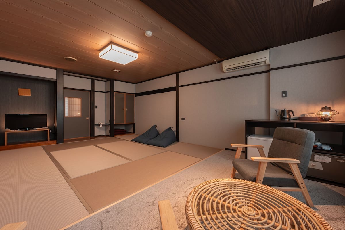 A traditional Japanese-style room with tatami flooring, a television, a desk with a lamp, and a chair.