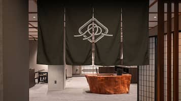 Un interior moderno con una mesa de madera central, un estandarte negro con un logo blanco y un separador de estilo japonés tradicional.