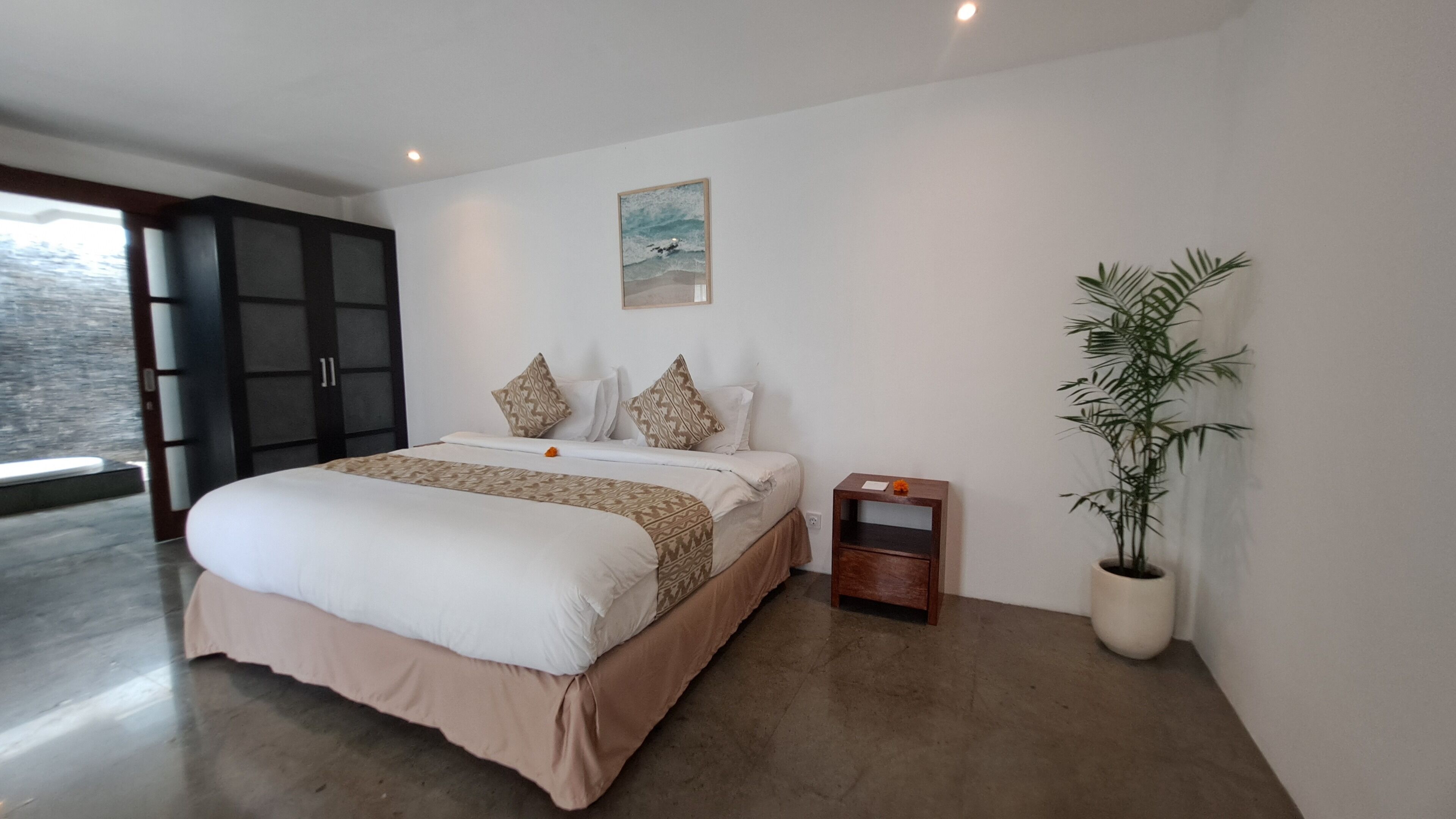 Een moderne slaapkamer met een groot bed, een nachtkastje, een potplant en een schilderij aan de muur.
