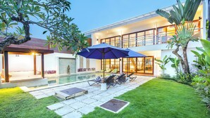 Une maison moderne dotée d’une piscine, d’un espace salon extérieur et d’une végétation luxuriante.