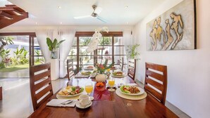 Un coin repas avec une table en bois mise pour le petit-déjeuner, entourée de chaises, et donnant sur un paysage verdoyant.