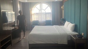 A hotel room with a large bed, a desk, a chair, a TV, and a window with curtains. - Duc Chung Hotel Ha Long (Bai Chay)