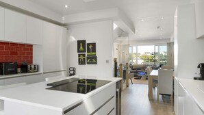 A modern kitchen with a central island, white cabinetry, and a red backsplash. There is a dining area with a table and chairs, and a view of the outdoors through large windows. - Bright & Modern Townhouse, Private Parking (Cornwall)