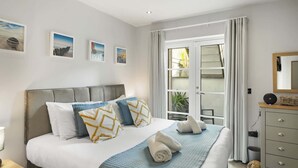 A bedroom with a bed, pillows, a bedside table, a dresser, a mirror, and a window with curtains. - Bright & Modern Townhouse, Private Parking (Cornwall)