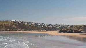A beach with a sandy shore and waves. There are houses on a hill in the background. - Bright & Modern Townhouse, Private Parking (Cornwall)