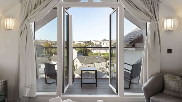A bedroom with a large window, a balcony, and a view of the neighborhood. - Bright & Modern Townhouse, Private Parking (Cornwall)
