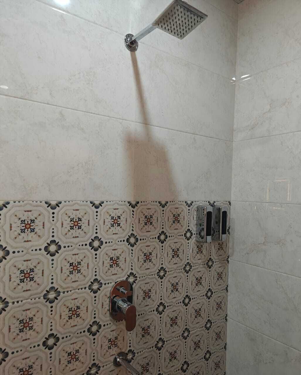 A shower area with a square showerhead, a wall-mounted faucet, and a tiled wall with a geometric pattern.