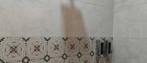 A shower area with a square showerhead, a wall-mounted faucet, and a tiled wall with a geometric pattern.