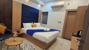 A modern hotel room with a bed, a chair, a small table, and a nightstand. - BlueNeck Ayodhya-Near ShriRam Mandir (Faizabad)