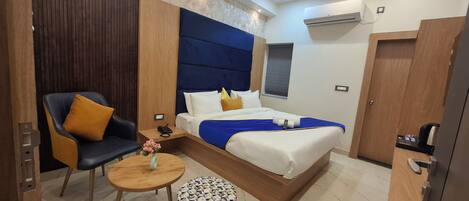 A modern hotel room with a bed, a chair, a small table, and a nightstand.