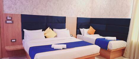 A hotel room with two beds, each with a blue bedspread and white linens. There are wooden headboards and a marble-patterned wall.