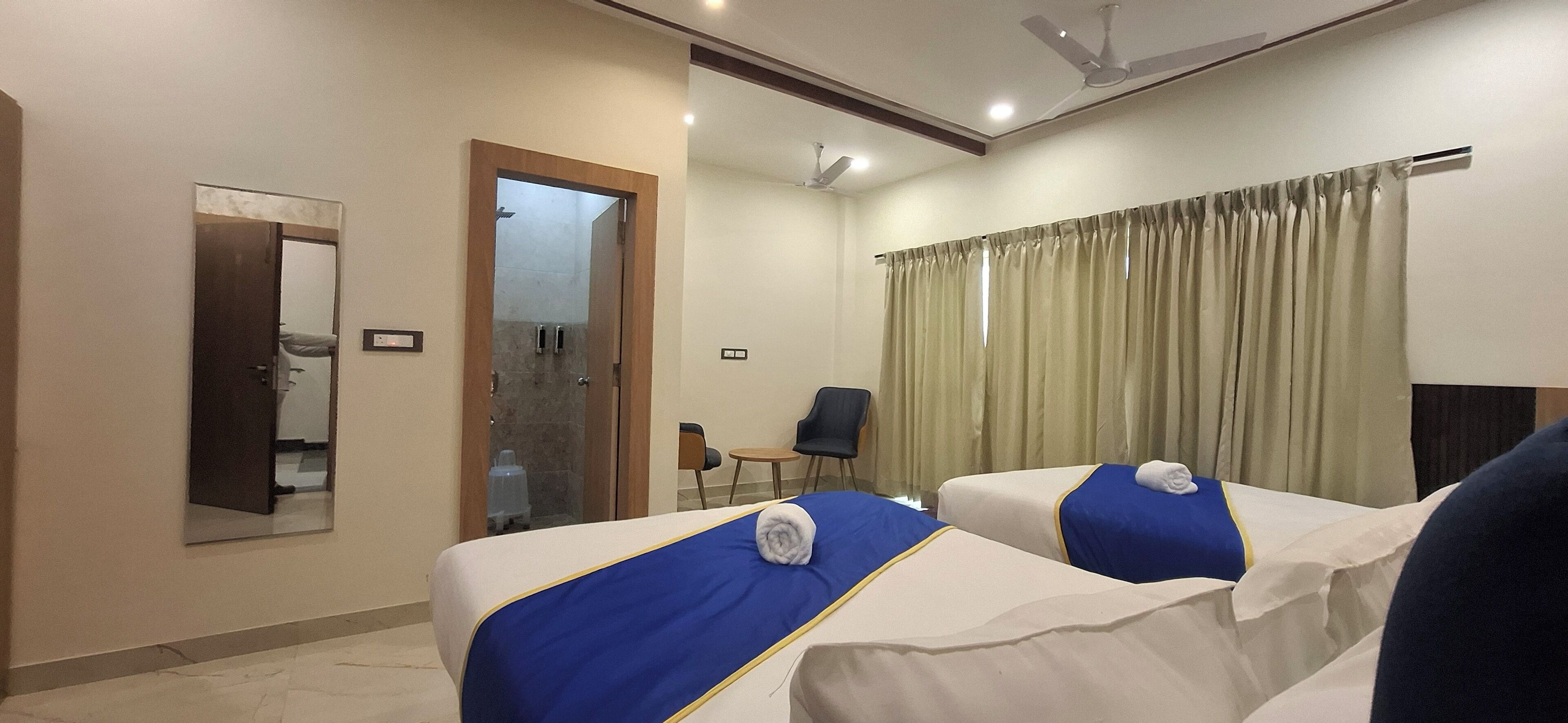 Una camera d'albergo con due letti, una zona doccia, una sedia e un'ampia finestra con tende.