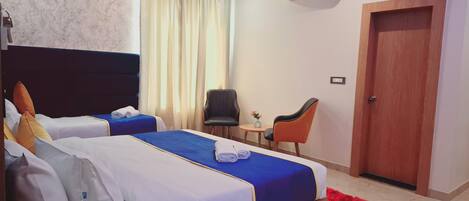 A hotel room with two beds, a wooden door, a small table with a vase, and two chairs.