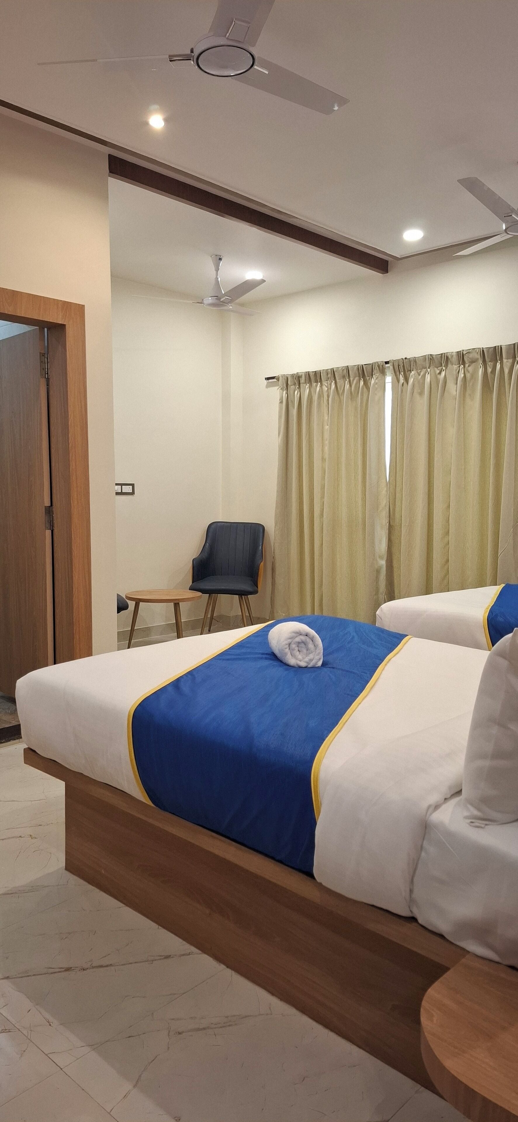 A hotel room with a bed, a chair, a small table, and a curtain.