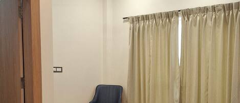 A hotel room with a bed, a chair, a small table, and a curtain.