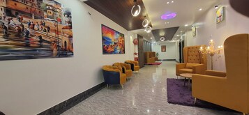 A hotel lobby with a marble floor, yellow and blue chairs, and artwork on the walls.