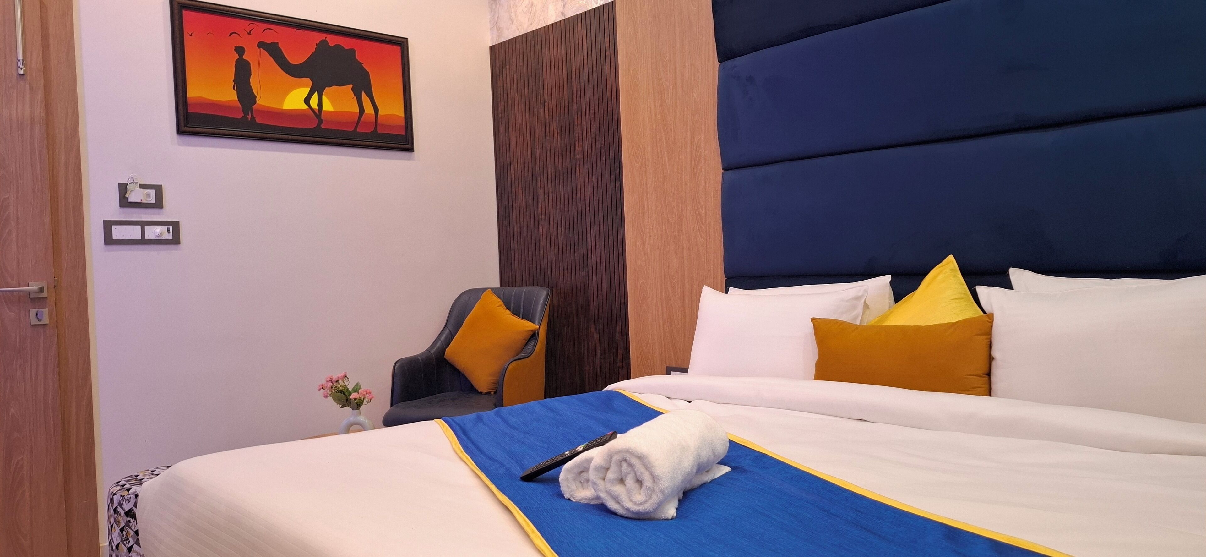Une chambre d’hôtel avec un lit, une chaise, un tableau et un vase de fleurs.