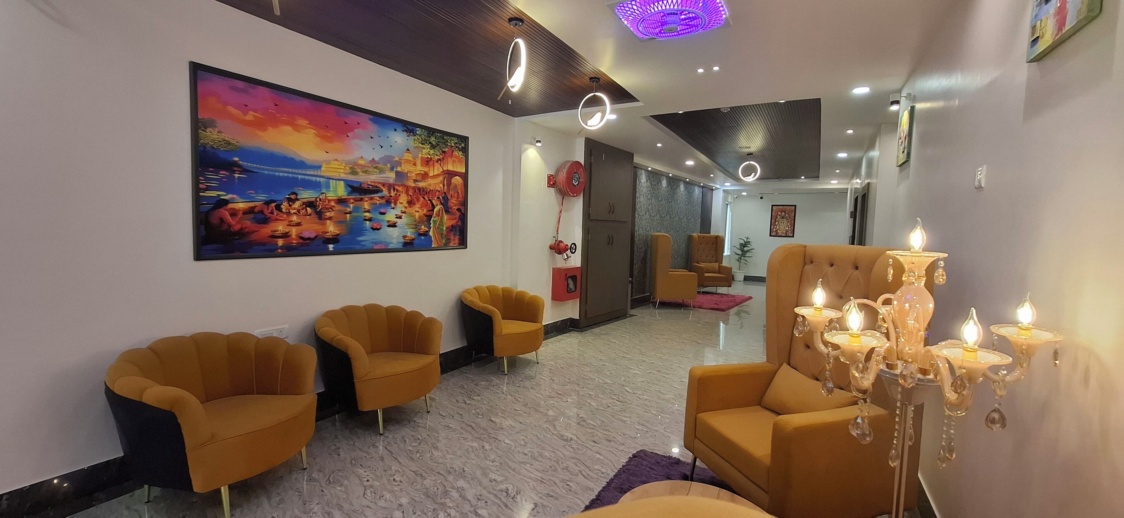 A modern lobby with a large painting, three yellow armchairs, a chandelier, and a marble floor.