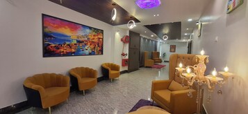 A modern lobby with a large painting, three yellow armchairs, a chandelier, and a marble floor.