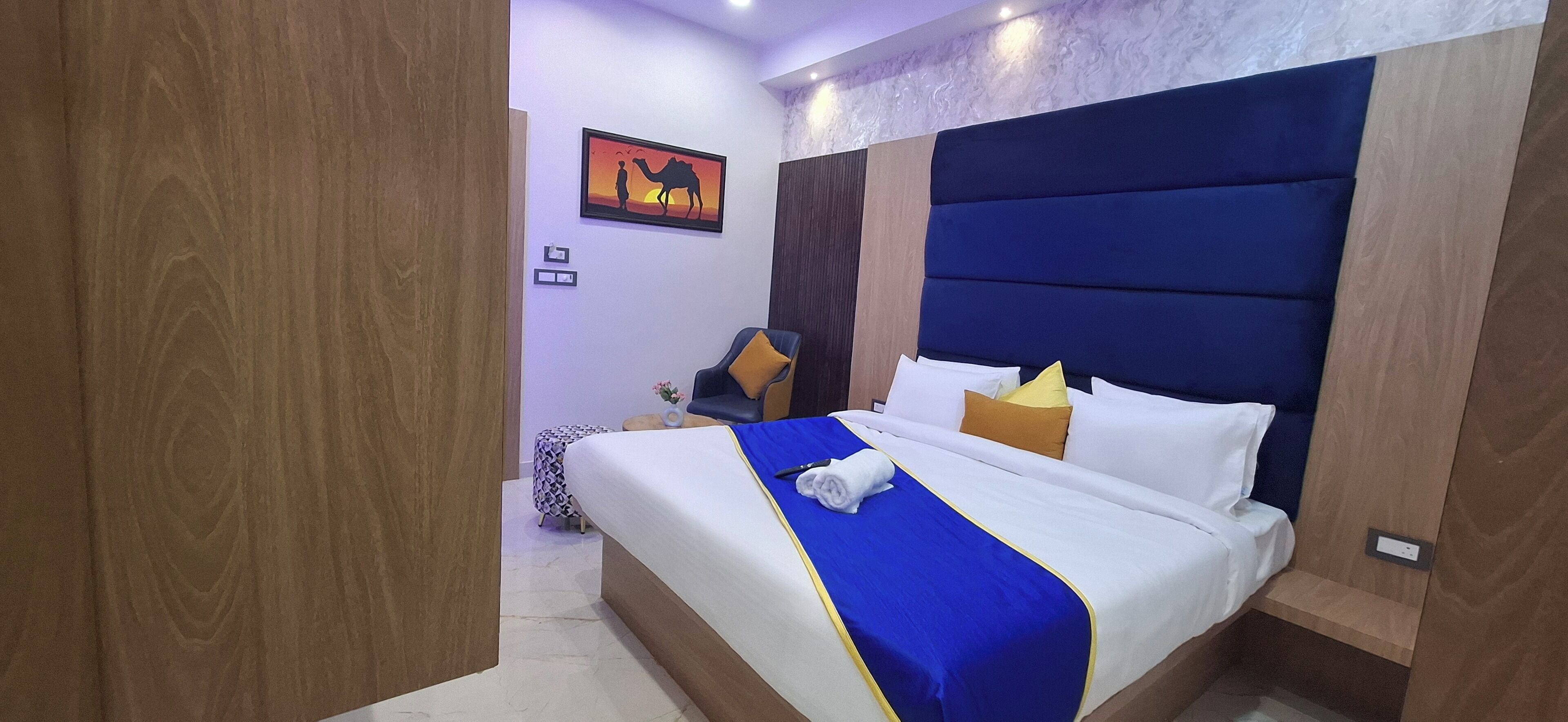 Un letto rifatto con una coperta blu e bianca, una testiera con un pannello blu e un comodino con una lampada.
