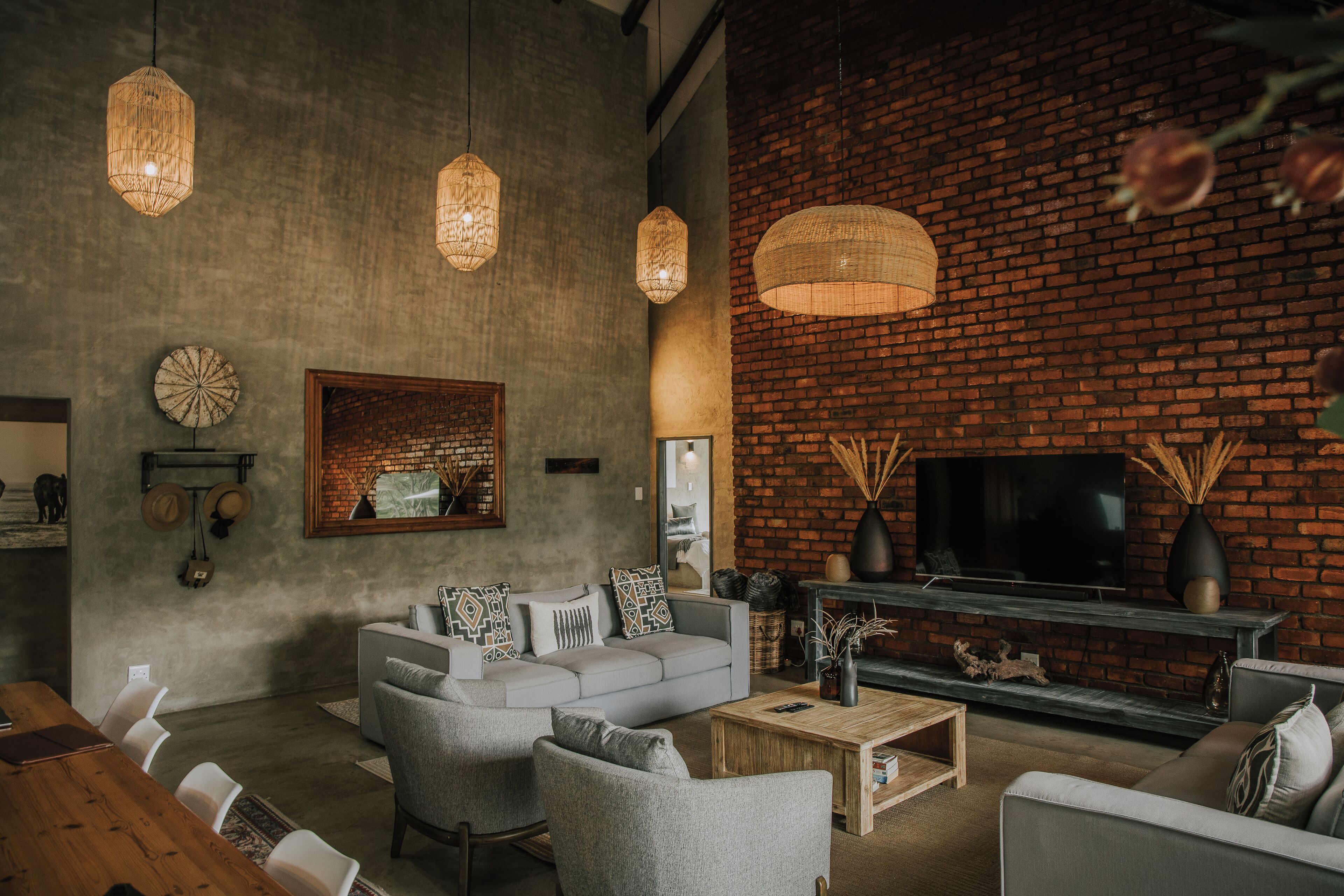 A modern living room with a brick wall, a sofa set, hanging lights, and a flat-screen TV.