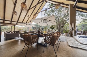 An open-plan dining area with wicker chairs, a central table set for a meal, and large umbrellas providing shade.
