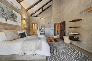 A modern bedroom with a large bed, a wooden ceiling, and a view into the living area.