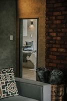 Una habitación con una cama, un espejo, un sofá gris y una pared de ladrillo.