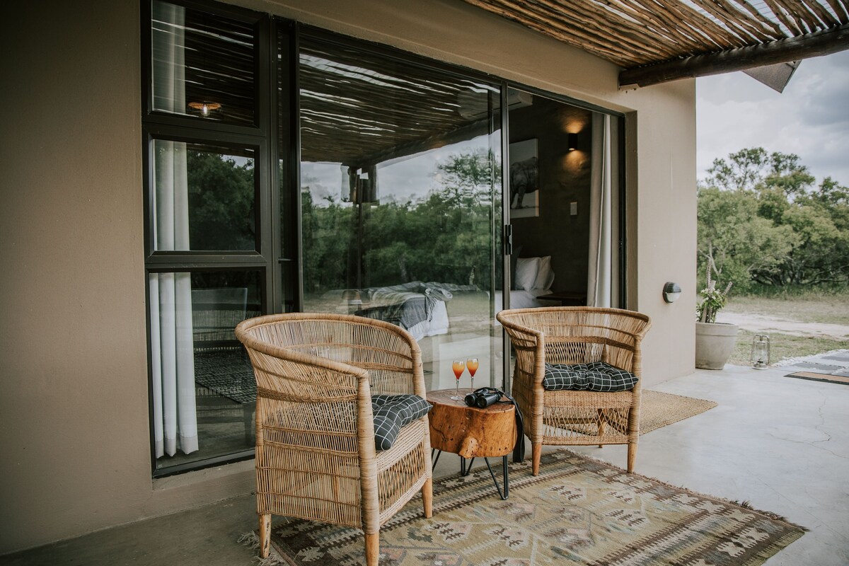 Une terrasse avec des chaises en osier et une petite table, une porte vitrée donnant sur un balcon, et une plante en pot.