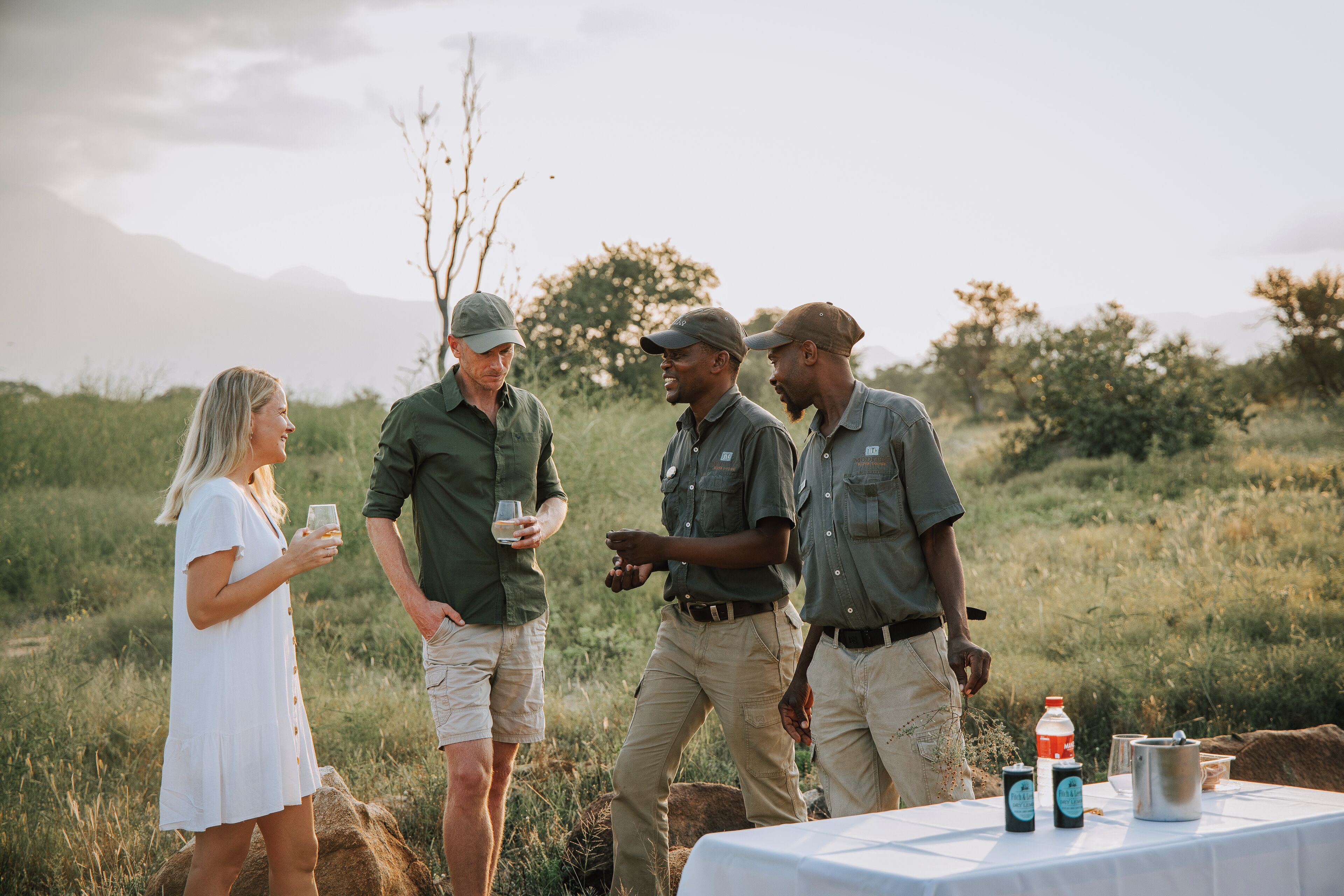 A group of people standing outdoors with a table that has bottles and a pot on it.