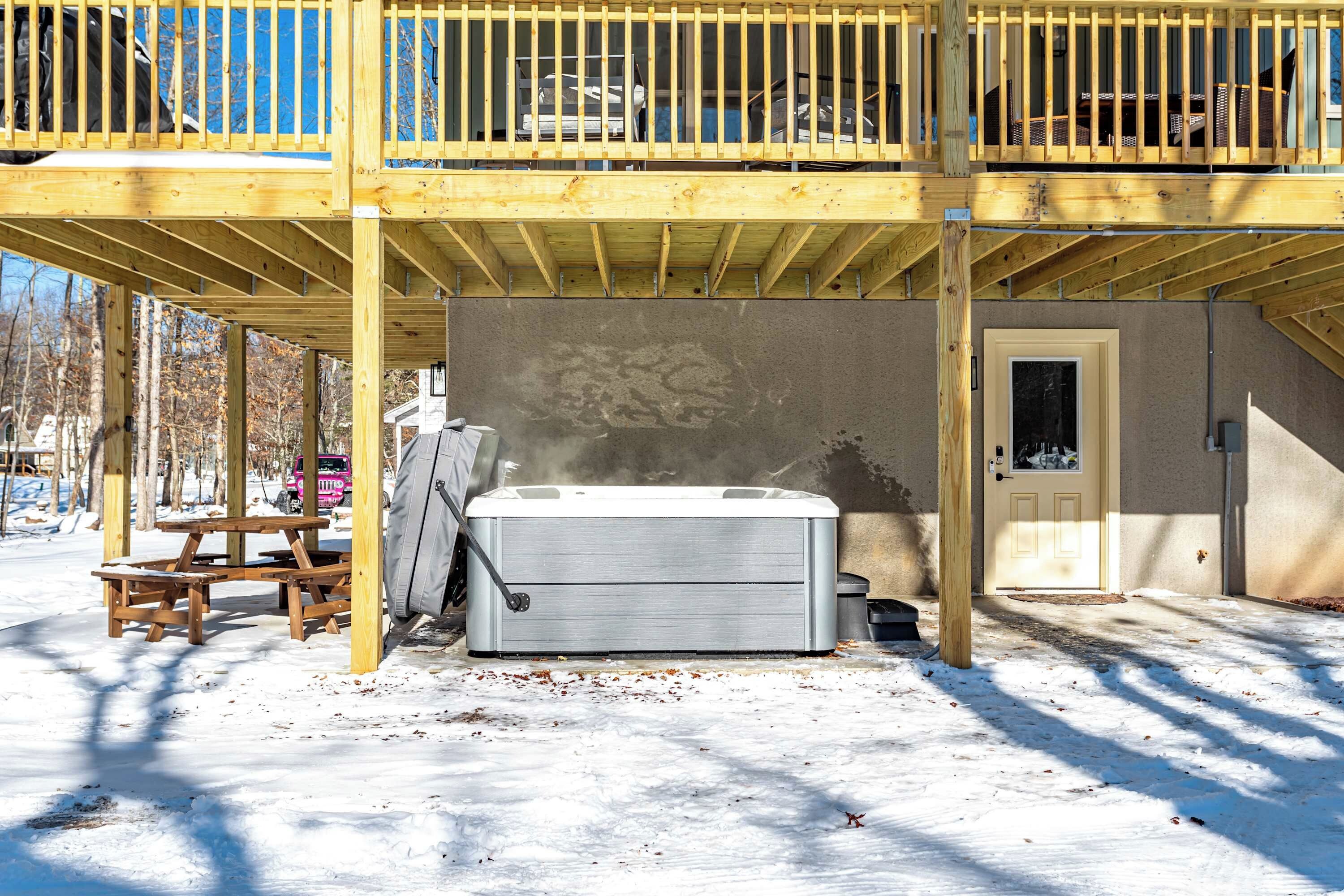Ein Whirlpool unter einer Holzdielen-Terrasse mit einer Steinwand und einer Tür.