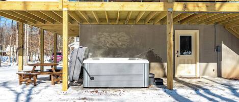 Ein Whirlpool unter einer Holzdielen-Terrasse mit einer Steinwand und einer Tür.