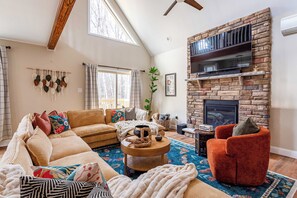 Un salon chaleureux avec une cheminée en pierre, un grand téléviseur et des fauteuils confortables.