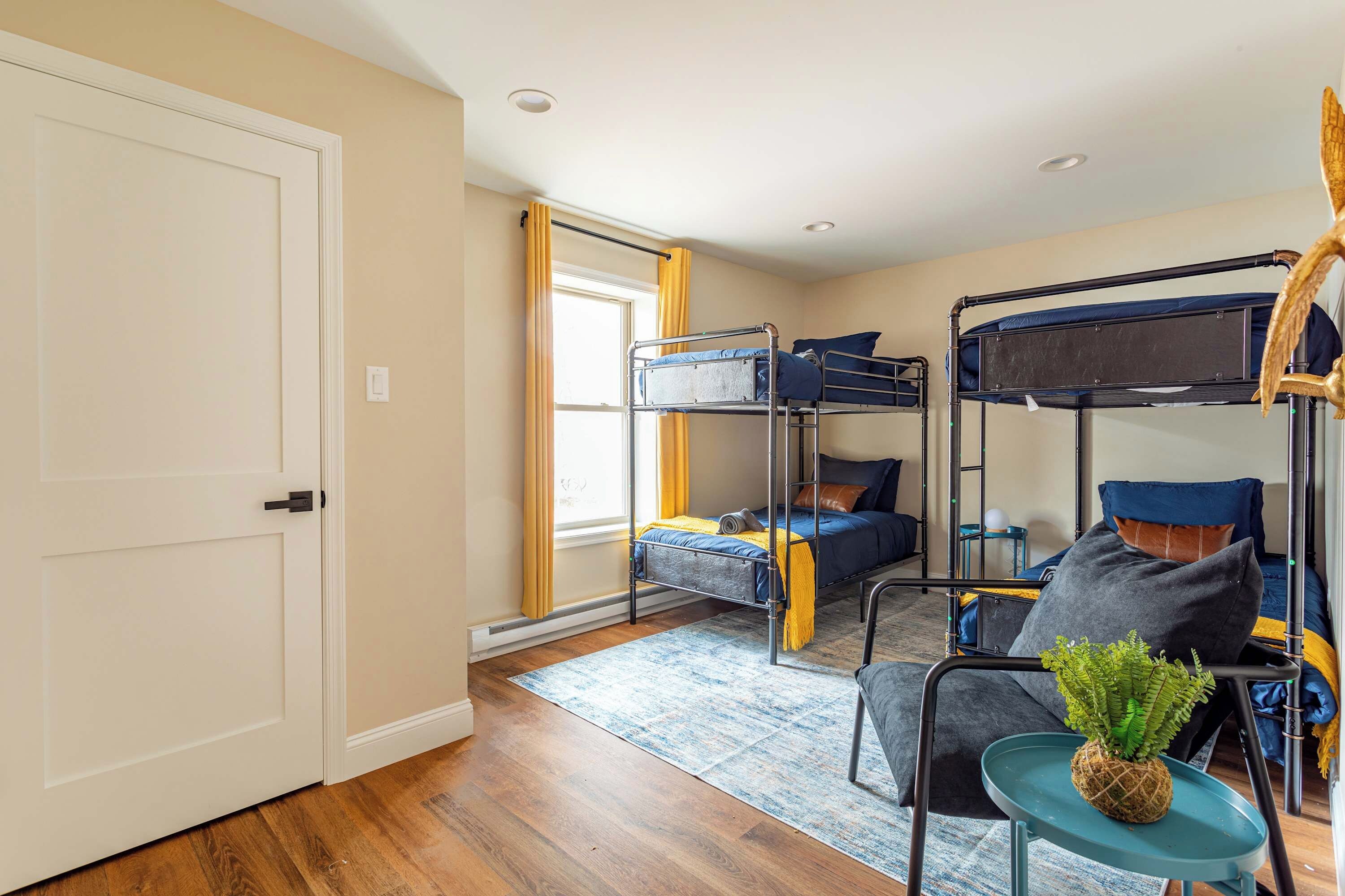 A dormitory room with bunk beds, a small table with a plant, and a window with curtains.