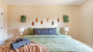 A neatly made bed with a green quilt, two pillows, and a folded blanket. There are two bedside lamps and a small plant on the wall.