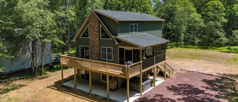 A two-story cabin with a balcony, a covered porch, and a dirt driveway.