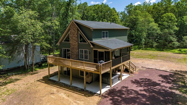 A two-story cabin with a balcony, a covered porch, and a dirt driveway.