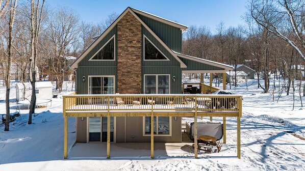 A two-story house with a balcony, a stone facade, and a snow-covered yard.