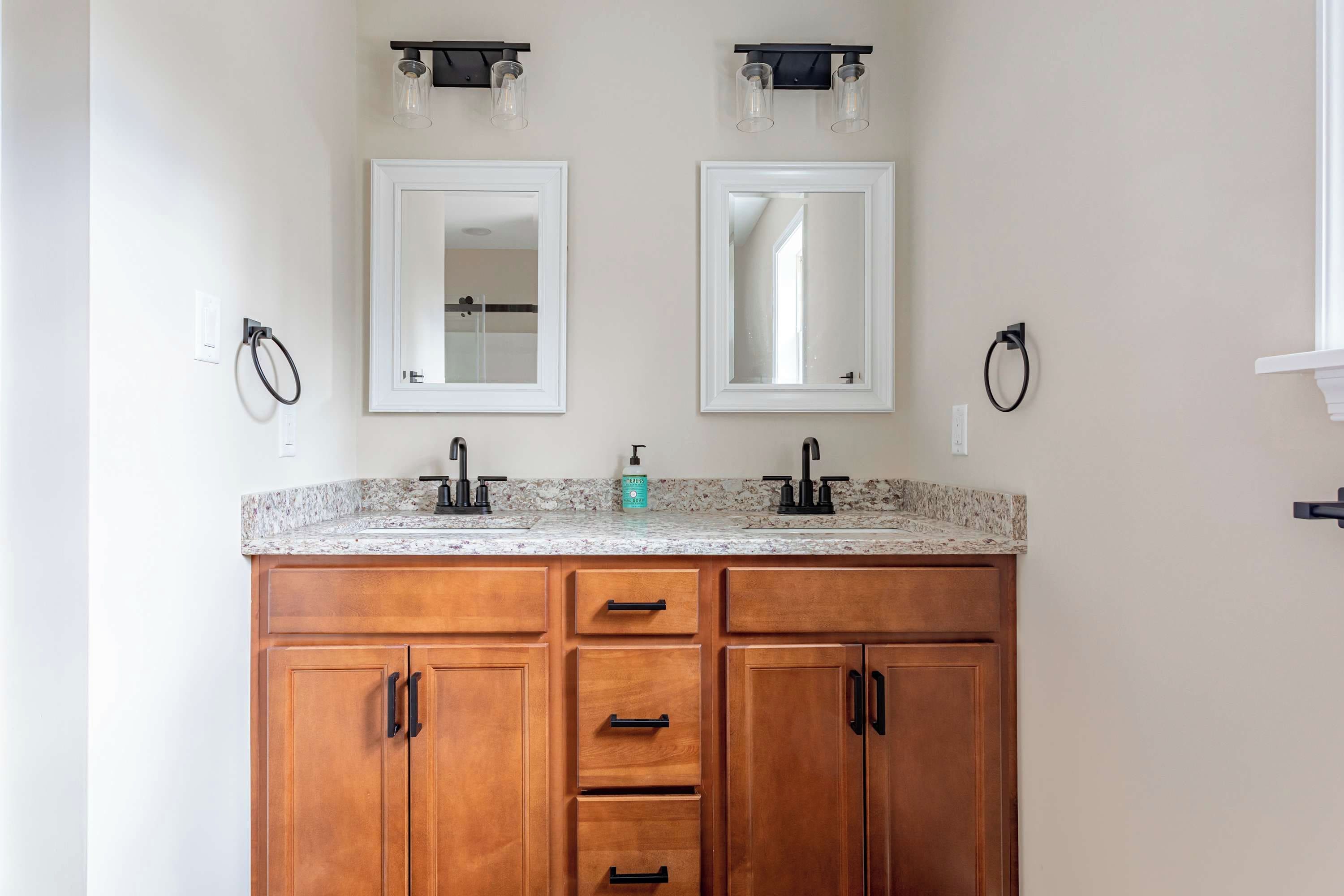 A bathroom with two sinks, wooden cabinets, and a granite countertop.