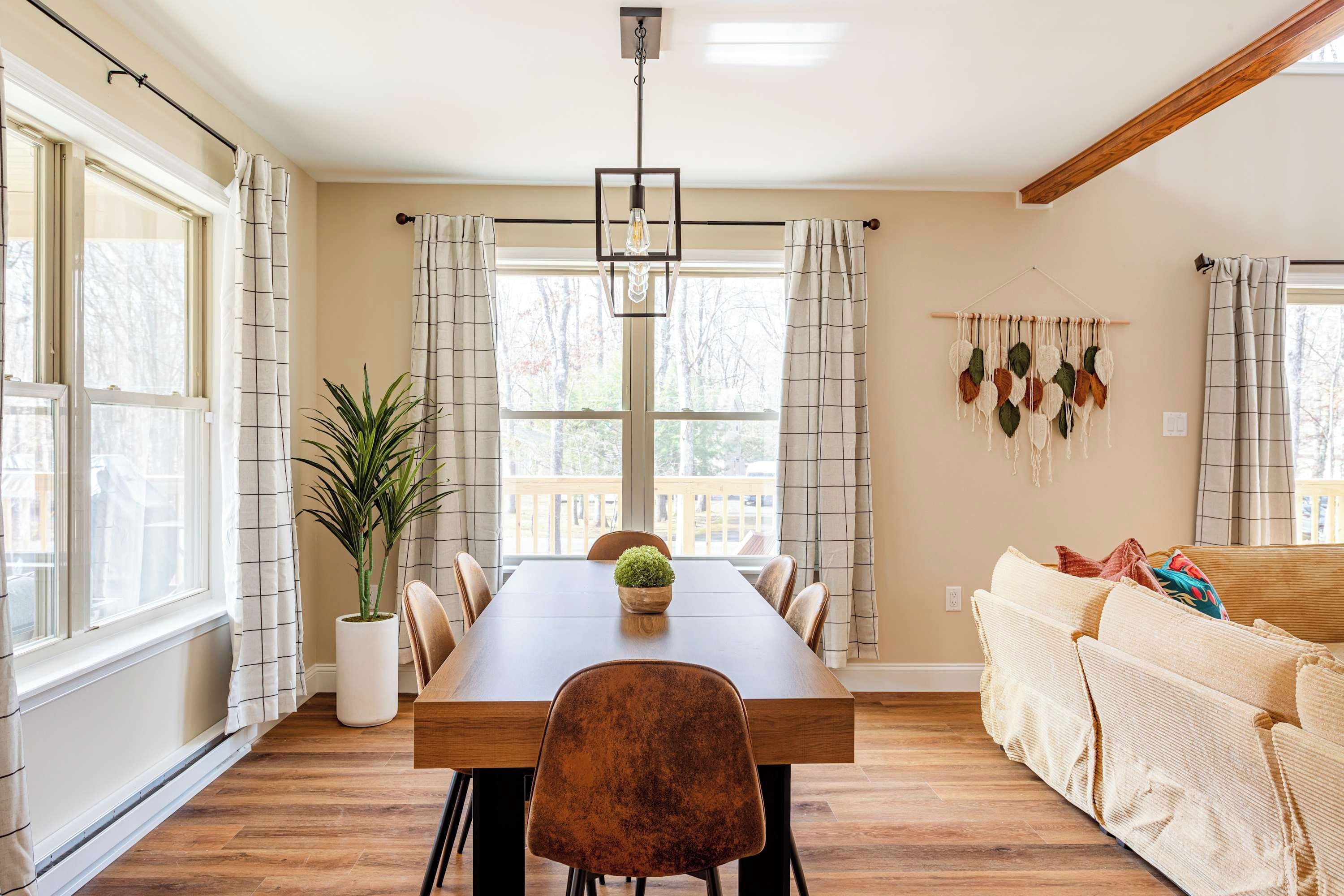 A dining area with a wooden table, chairs, a potted plant, and a hanging macrame wall decoration.