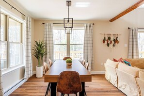 A dining area with a wooden table, chairs, a potted plant, and a hanging macrame wall decoration.