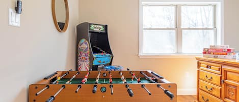 A room with a foosball table, a cabinet with drawers, a window, and a wall-mounted mirror.