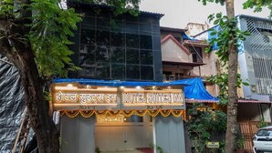 L’entrée d’un hôtel, avec une enseigne en hindi et en anglais, une bâche bleue recouvrant l’entrée, et un panneau indiquant « Stationnement interdit ».