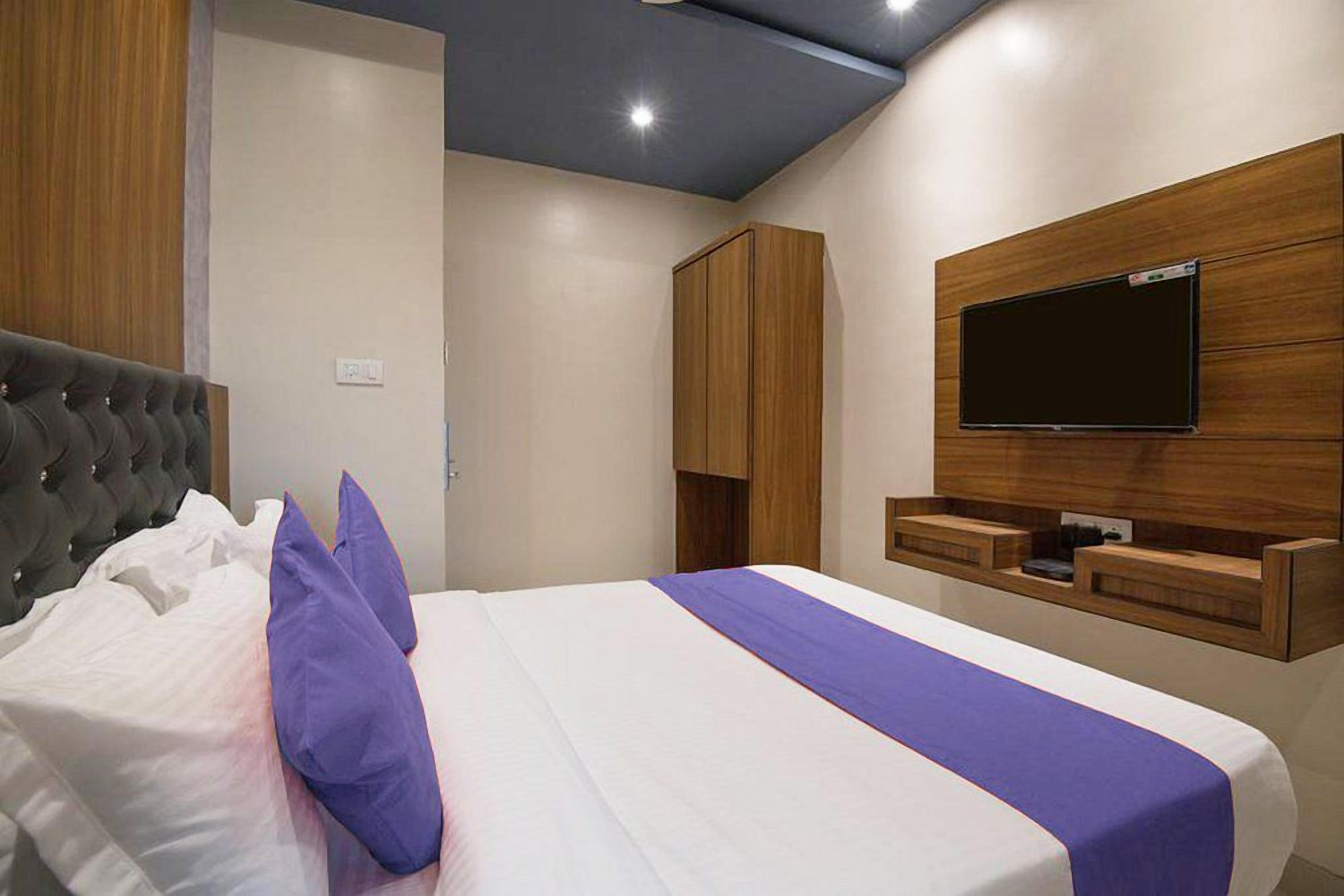 A modern hotel room with a large bed, a flat-screen TV mounted on the wall, and wooden cabinetry.